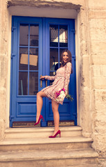 Elegant brunette model in trendy dress holding bouquet of flowers. Woman posing at the door.