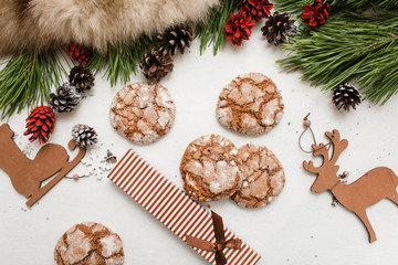 Festive background of Christmas and New Year. Decoration from pine branch with strobila, wooden deer and skate, sweet cakes and present, top view. Holidays, congratulation and homemade decor concept