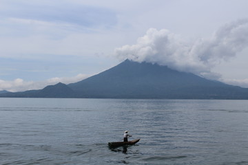Uomo da solo sulla sua barca che naviga sul lago e sullo sfondo un vulcano, Atitlan, Guatemala