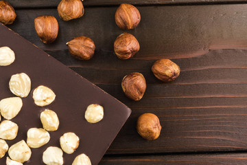 Part of bitter dark chocolate bar with hazelnut on wooden planks background, top view