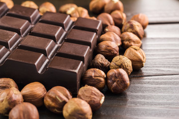 Part of bitter dark chocolate bar with hazelnut on wooden planks background, close-up view