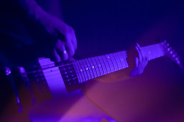 Electric guitar player on a stage with colorful blue and purple scenic illumination