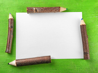 Blank sheet of paper and wooden pencils on green background