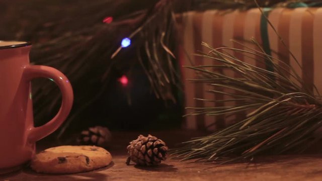 Christmas festive composition in motion. Close up of wrapped present, cup of drink and chocolate scones on illuminate fairy lights background. Family celebration and New Year traditions concept
