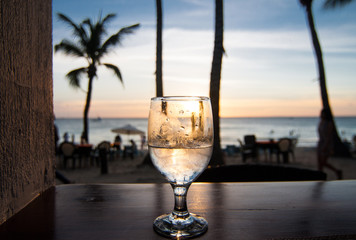 Glass of wine on the sunset. Palms and sea on the background.