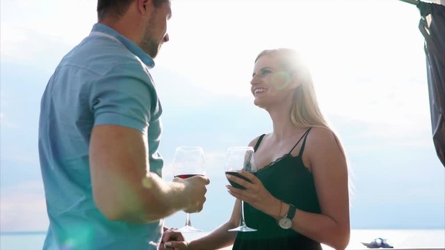 A loving couple is lovely gazing into each others eyes while talking. They are holding glasses of wine and leaning on the railings.