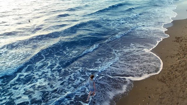 Aerial Shot of a Woman Walking on the Seashore of the Warm and Majestic Sea/ Ocean. Shot on a Camera in 4K (UHD).