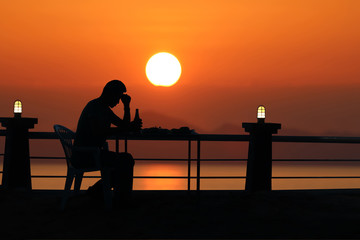 Fototapeta na wymiar Silhouette sad man drinking beer at the beach with red sky sunset
