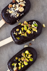 Flat lay with chocolate glazed and pistachios popsicle ice-creams on dark table. 