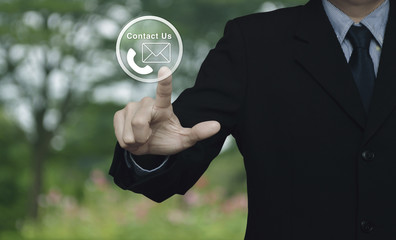 Businessman pressing telephone and mail icon button over blur flower and tree in park, Contact us concept