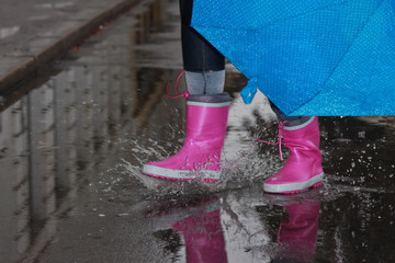 Person with pink boots and blue umbrella splashing in the puddle