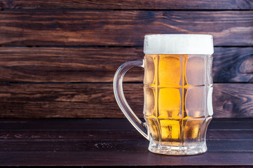 glass of cold frothy lager beer on old wooden table