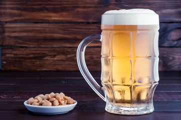 glass of cold frothy lager beer and peanuts plate on wooden table