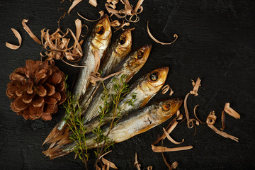 Smoked baltic herring with filings, pine cone and thyme on dark stone table. Top view, flat lay, closeup.
