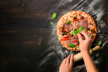 Girl hands making, decopating, preparing pizza with basil leaves on dark background. Top view, copy...