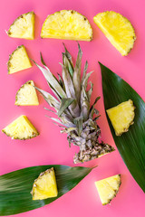 Tropical fruits background. Pinneapple slices in front of big leaves on pink background top view