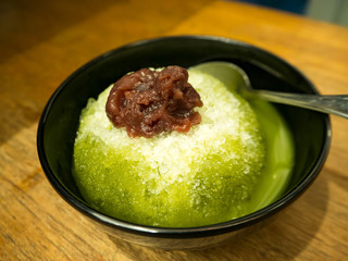 Macha green tea shaved ice with red beans. Traditional Japanese sweet Dessert in black bowl.
