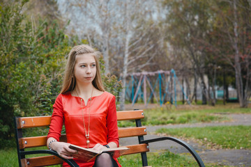 The girl reads the book in the park. The girl in the park sits on a shop. Walk on the park in the summer.