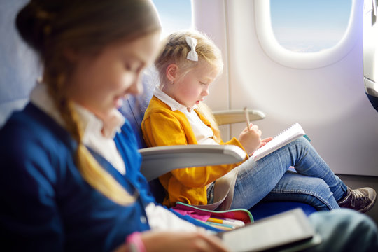 Adorable little girls traveling by an airplane. Child sitting by aircraft window and drawing a picture with colorful pencils. Traveling with kids.