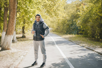 Happy man sportsman smiling with a bottle of water in a track suit in a sunny autumn day outdoors in a blurred park landscape. Sports and fitness. The concept of a healthy lifestyle.