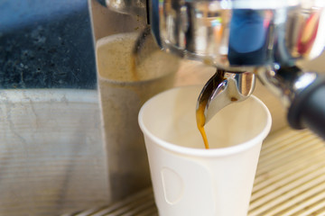 Close up of espresso coffee pouring from coffee maker machine to white paper glass shot. barista coffee brewing concept.