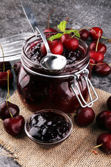 Jar of cherry jam, sour cherries and spoon on grey vintage backg