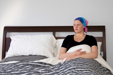 Young cancer patient in a headscarf looks out the window while resting in bed