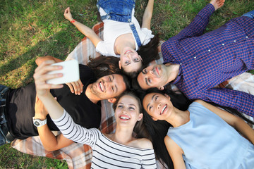Happy young friends lying on grass and taking selfie