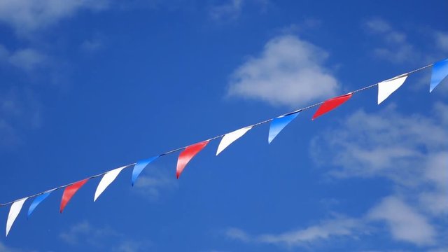 Multicolored summer Bunting flags blowing in the wind against a blue sky.