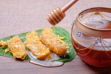 Honey dripping from wooden honey dipper and fried slices of the ripe BANANA also called Pisang Goreng, which are eaten as snack or used to accompany dishes in Malaysia