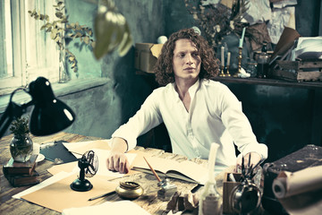 Writer at work. Handsome young writer sitting at the table and writing something in his sketchpad