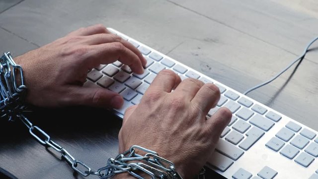 Businessman hands tied with chains on wrists typing on laptop keyboard