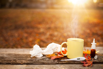Cup with tea, thermometer, autumn leaves, nose drops and paper tissues, flu season in autumn
