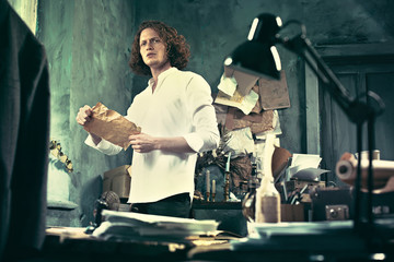 Writer at work. Handsome young writer standing near the table and making up something in his mind