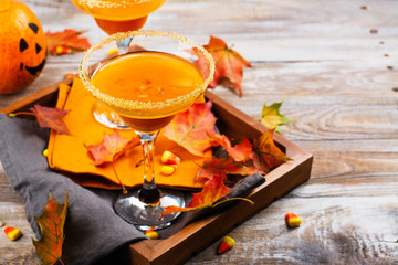 Autumn pumpkin martini cocktail with fall leaves on wooden tray. Copy space