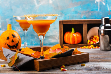 Autumn pumpkin margarita cocktail with halloween decor on wooden table. Copy space