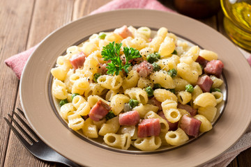 Pasta with green peas, onion, bacon and cheese on wooden background