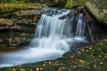 Waterfall falling on stones through autumn forest. Fall nature specification.