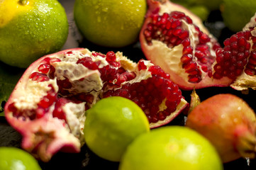 lemon on a branch and limes. chopped grenade. on a black background. dark photo. water drops. wet fruit