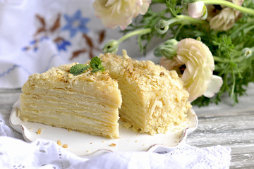 the cake is napoleon in a cut. against the background of vintage textiles. a bouquet of white flowers. sweet breakfast for the family.