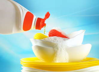 Concept washing-up. Liquid detergent for washing dishes. A drop of detergent falls dripping from a bottle on plates and a sponge on a blue background close-up.