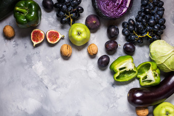 Fresh organic raw green and purple colored vegetables and fruits on stone background