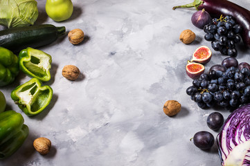 Fresh organic raw green and purple colored vegetables and fruits on stone background.