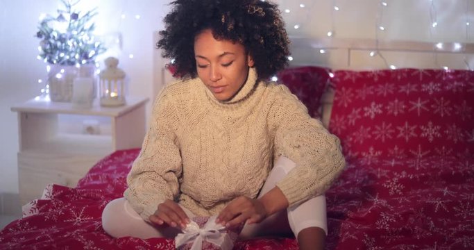 Single beautiful African woman with calm or cautious expression holding Christmas gift in bed