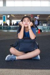 Teen girl sitting on airport floor with luggage, resting