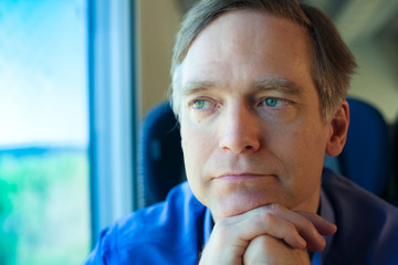 Caucasian male by train window chin on hand, thinking