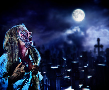 Undead zombie scary girl on halloween graveyard at night on dark clouds sky background. Woman in zombie apocalypse hunting outdoor. Behind monster cemetery with crosses. Moon comes out from clouds