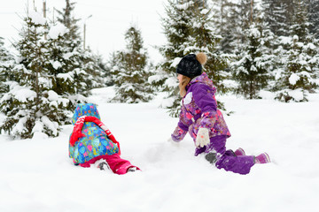 Fototapeta na wymiar Girl with little sister playing in the snow among the pine trees