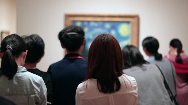 People looking at a work of art. Public starring at a painting at a museum. Group of people contemplating a work of art