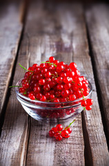 Red currants in shiny glass bowl on white rustic old wooden table in studio